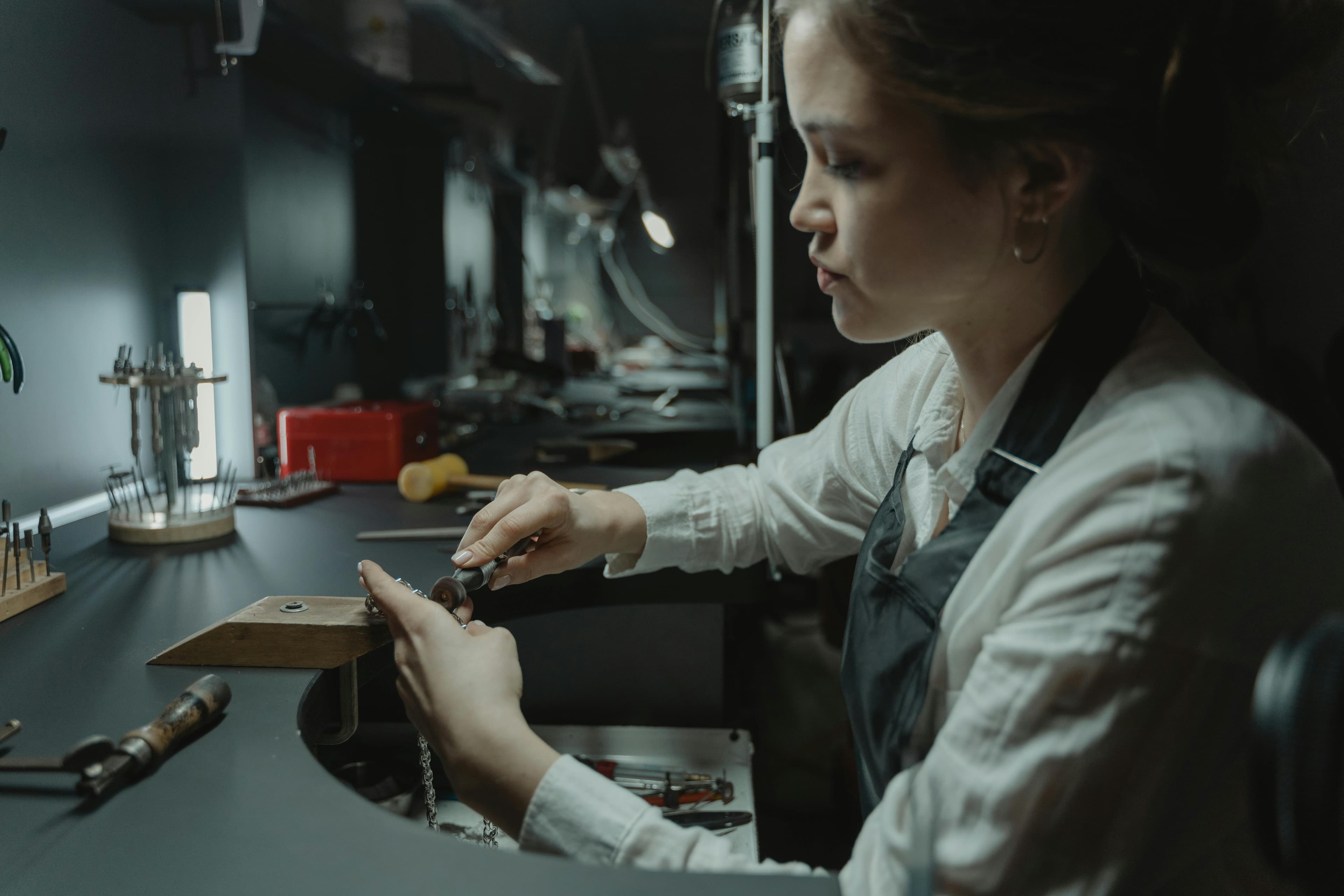 Jeweler crafting a chain piece at a dark workbench